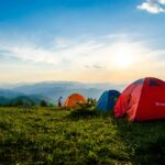 Vibrant tents on a grassy mountain ridge with a stunning sunrise view, ideal for adventure.